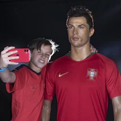 En pojke tar en selfie med en vaxfigur av en fotbollsspelare i en Portugal-tröja, båda bär röda skjortor.