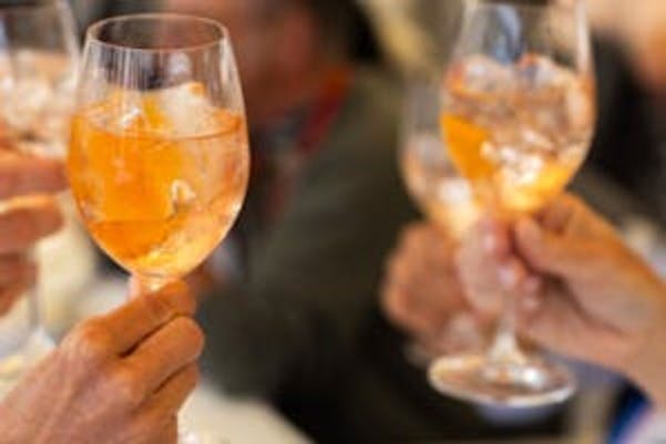 Close-up van verschillende handen die glazen met ijs en een oranje drankje vasthouden en samen proosten.