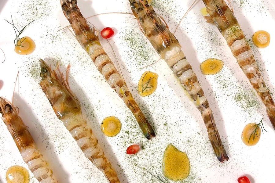 ハーブ、イエローソースのドロップ、小さな赤い飾りが付いた白い表面に並べられた調理されたエビ。