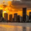 Der goldene Nachthimmel schmiegt sich an die Skyline von Miami und wirft eine helle Reflexion auf das ruhige Wasser.