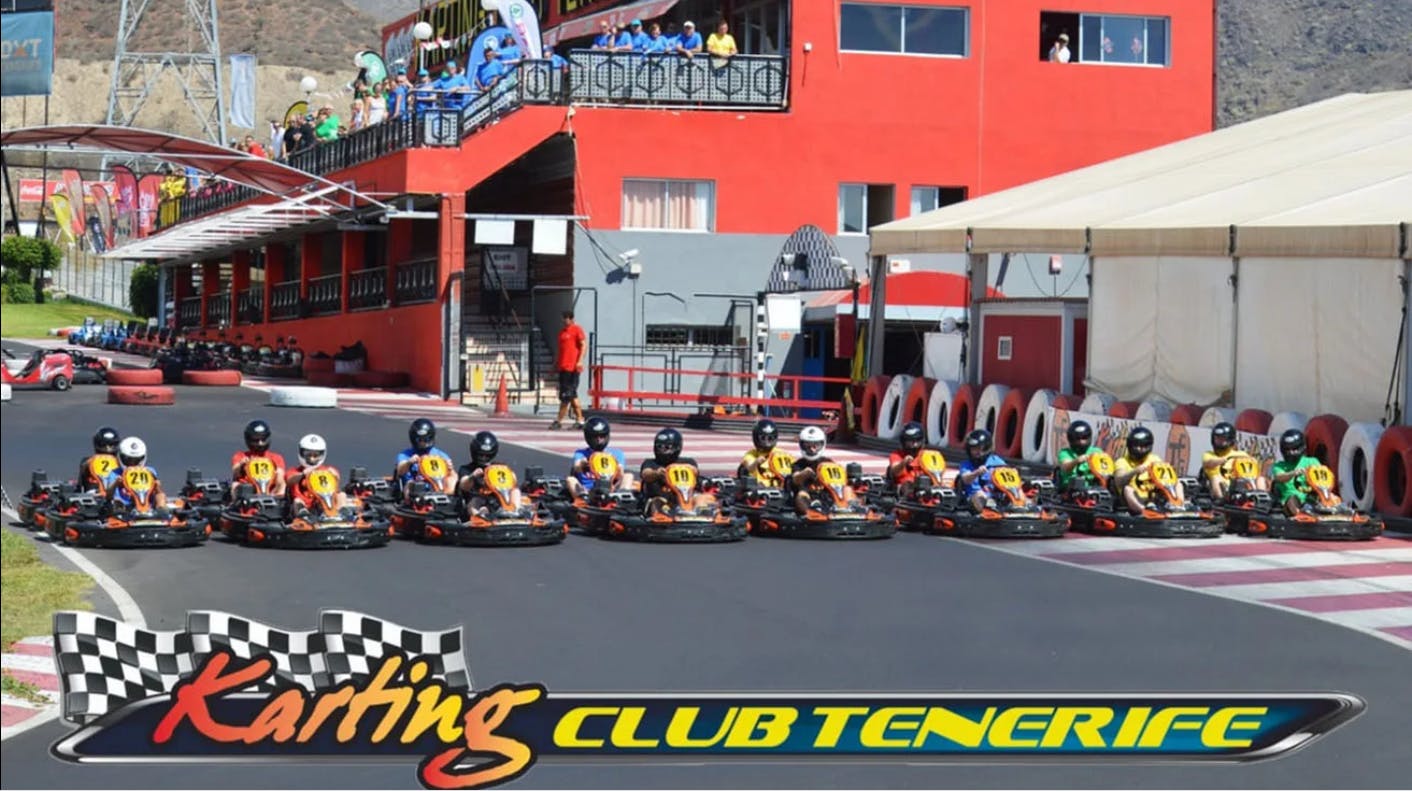 En række gokartkørere iført nummererede trøjer på startlinjen på Karting Club Tenerife-banen med tilskuere i baggrunden.