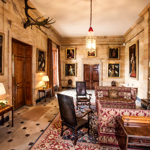 Elegant room with antique furniture, ornate rug, portrait paintings, a chandelier, candelabras on a mantel, and wooden doors.