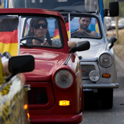 Flera personer kör veteranbilar i rad, var och en prydd med tyska flaggor. Den ledande bilen har ett gult leopardmönster.