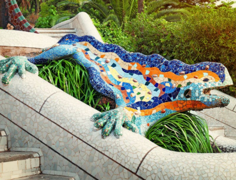 Sculpture de lézard en mosaïque colorée avec des carreaux bleus, verts et orange, intégrée dans un jardin à la végétation luxuriante.