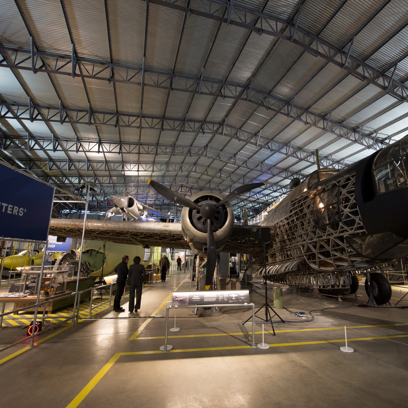 En stor hangar viser et dekonstrueret tomotorsfly, hvor folk observerer udstillingen.