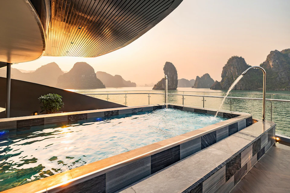 A rooftop pool overlooking a serene bay with limestone karst formations at sunset.