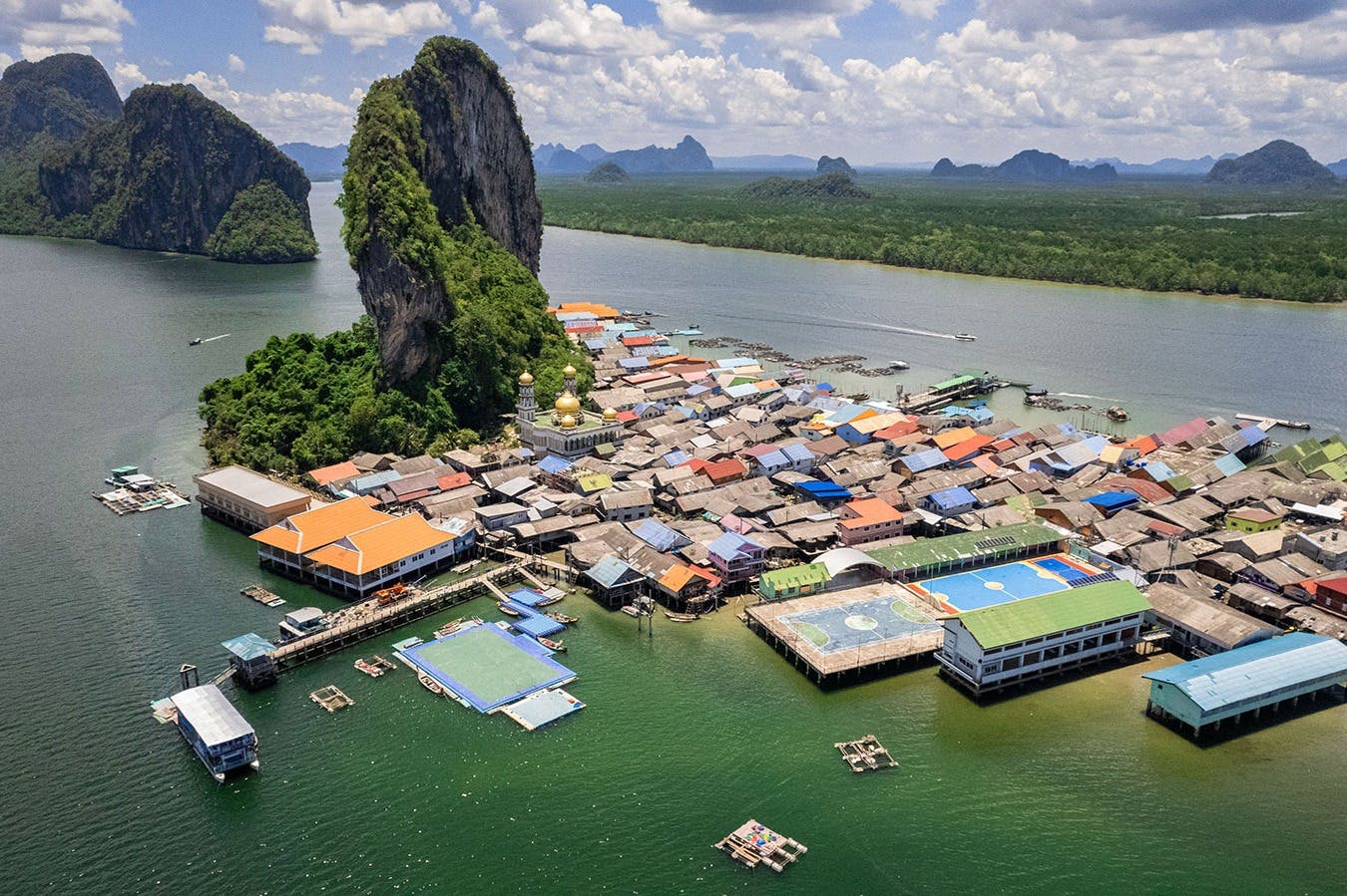 鸟瞰一个沿海村庄，屋顶五彩缤纷，周围环绕着多云的天空下的水和郁郁葱葱的绿色山脉。