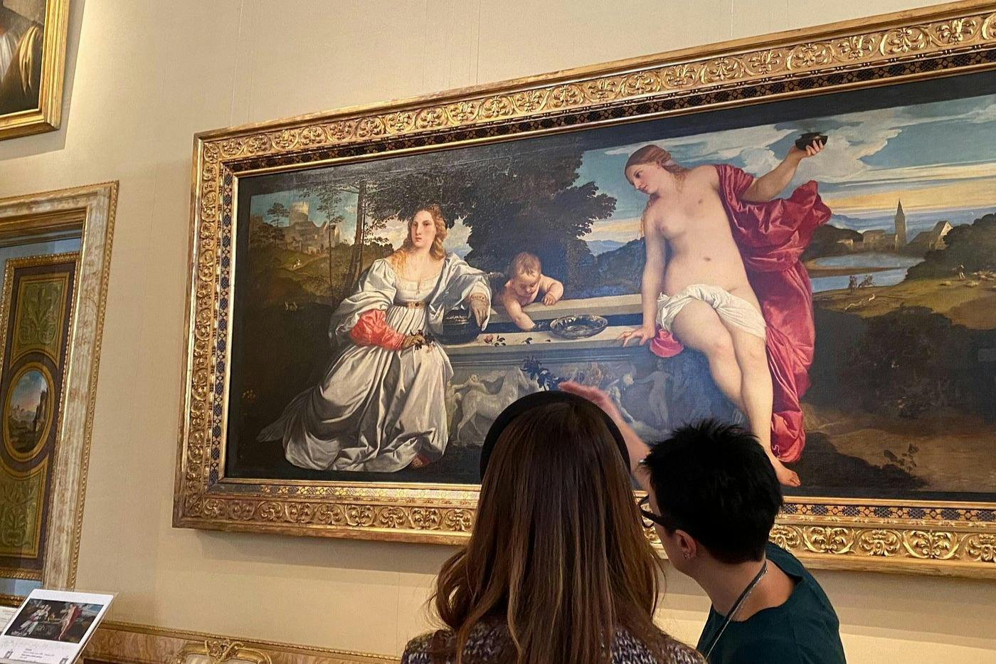 Two people observing a framed painting in a museum, depicting a classical scene with figures in a landscape.