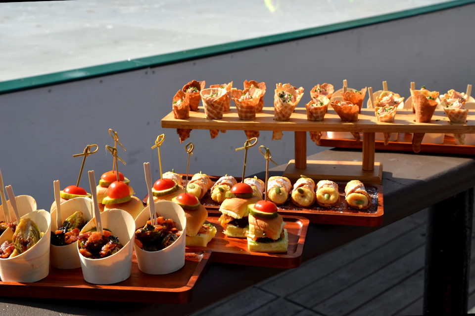 An assortment of gourmet appetizers, including sliders, skewered bites, and savory cones, displayed on wooden trays and stands.