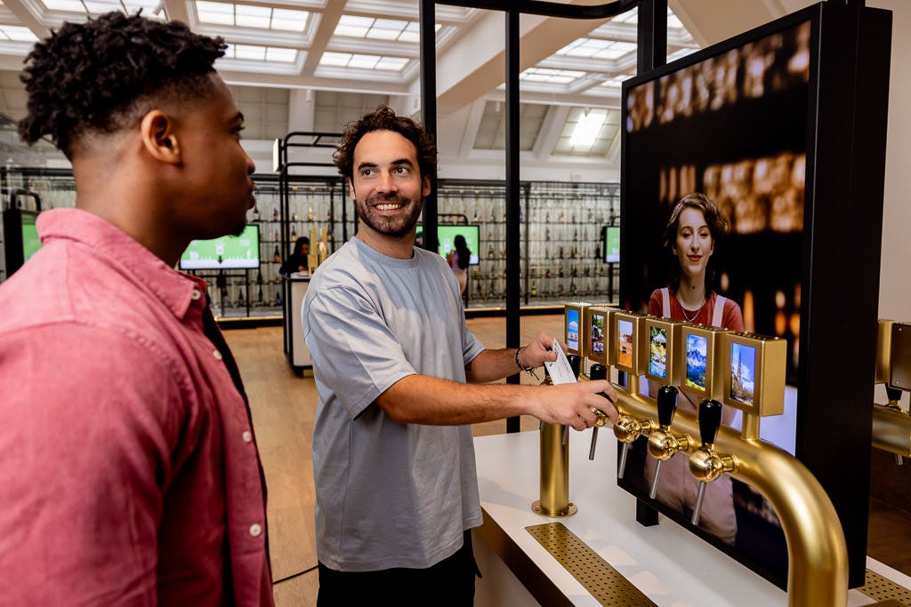 セルフサービスのビールタップの前に2人の男性が立ち、モダンで明るい空間で1人の男性が飲み物を注ぎながらもう1人と話しています。