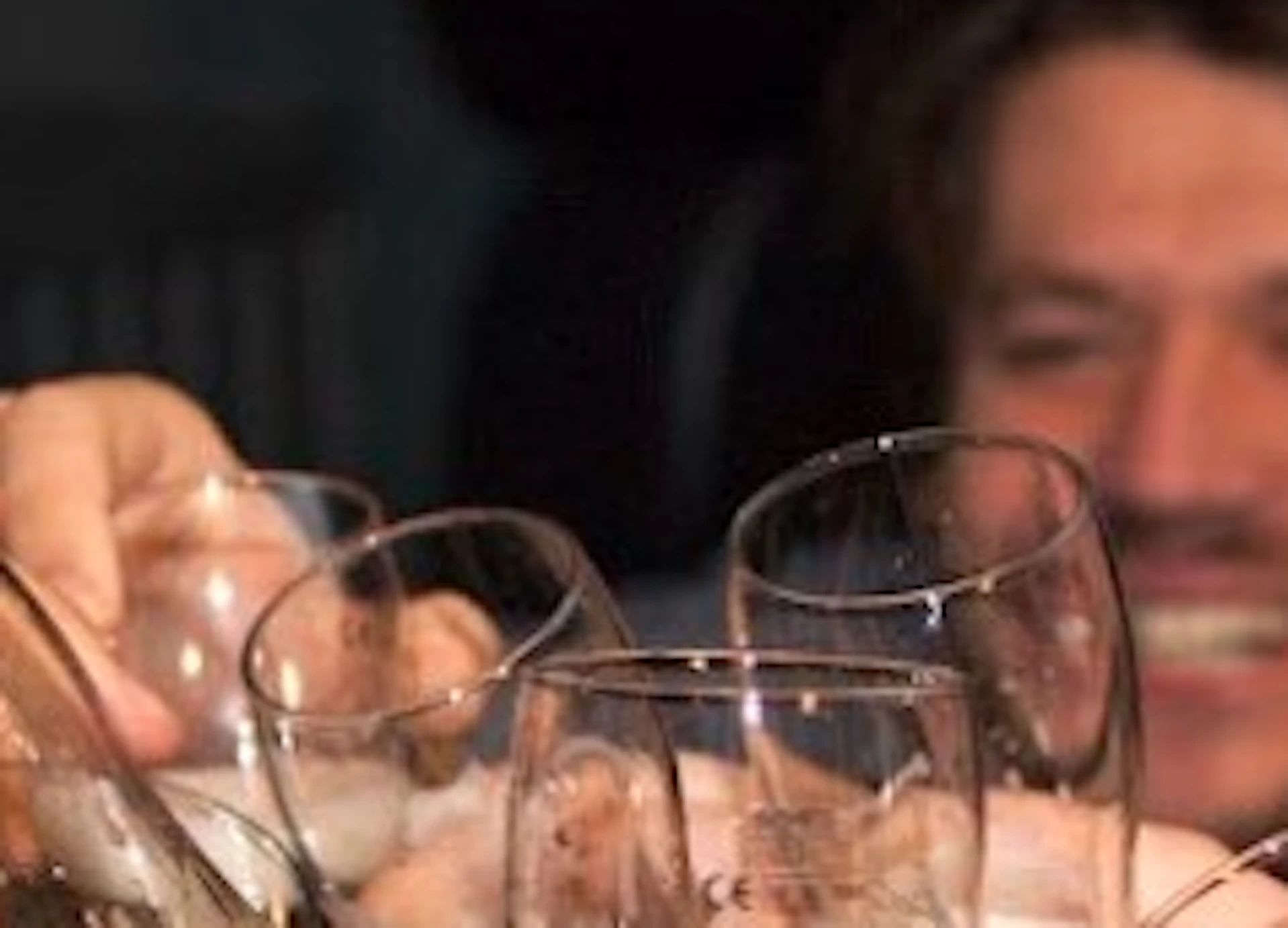 Group of people smiling and clinking beer glasses together, with bottles on a table in the foreground.