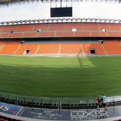 Panoramautsikt över en tom stadion med röda, gröna, orange och blå platser, och några personer som står vid planen.