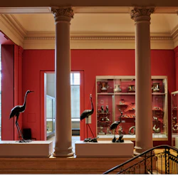 Museuminteriör med röda väggar, utställning av bronsfågelstatyer på piedestaler och glasfodral som visar olika silverartefakter.