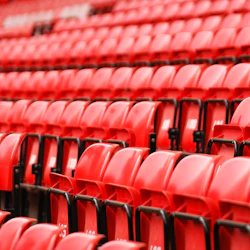 Rader av tomma röda stadionsäten med svarta metallramar, sett från en vinkel.