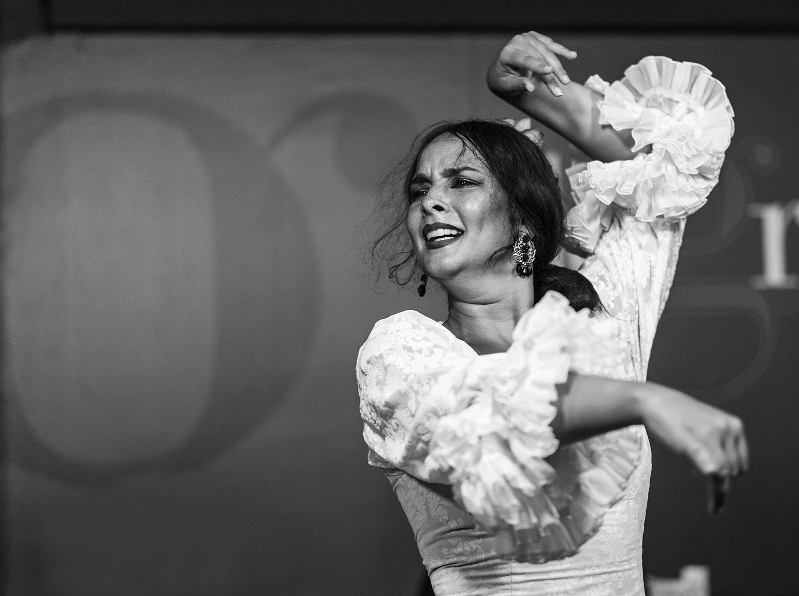 Une femme exécute une danse avec passion, vêtue d'une robe à volants et de boucles d'oreilles, l'expression intense et les bras levés.