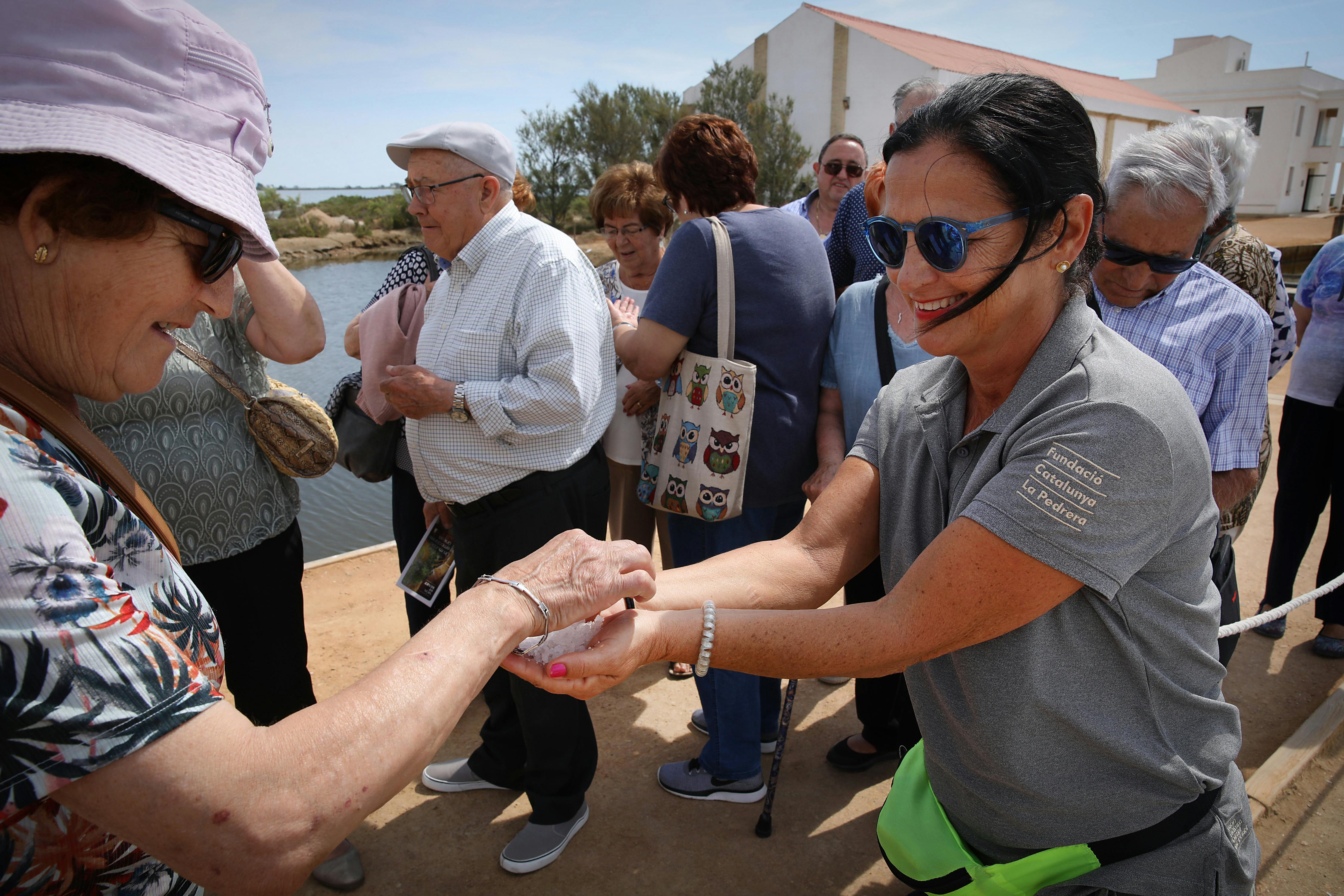 Μια ομάδα ηλικιωμένων ενηλίκων που στέκονται σε εξωτερικούς χώρους κοντά σε ένα υδάτινο σώμα. Ο ένας δίνει κάτι στον άλλον.
