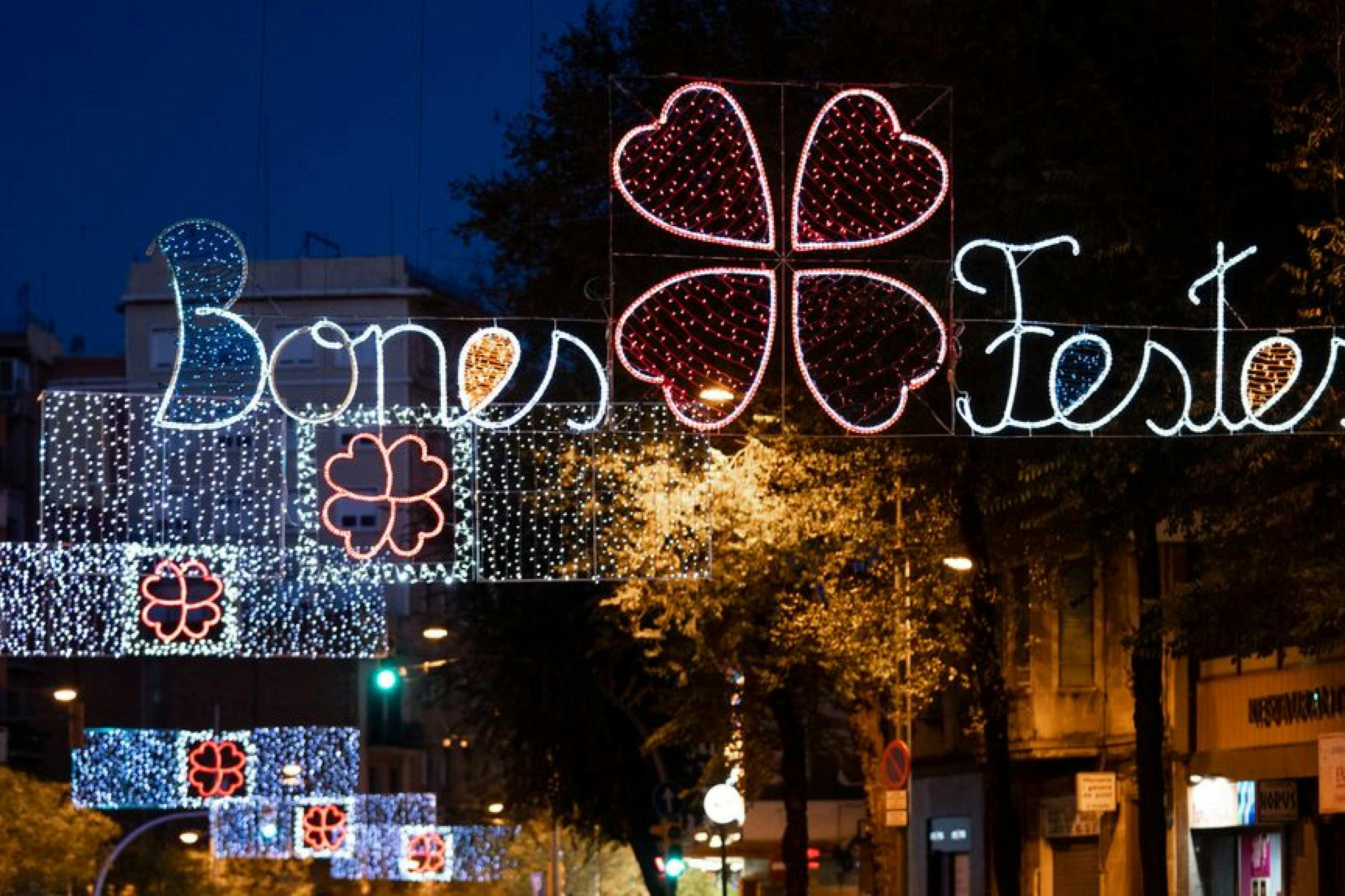 Festive street decorations with illuminated text "Bones Festes" and heart-shaped light displays at night.