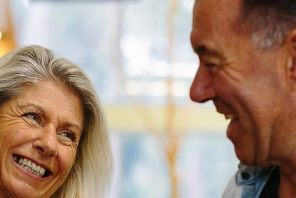 Two people smiling at each other indoors, one holding a small stuffed koala toy.