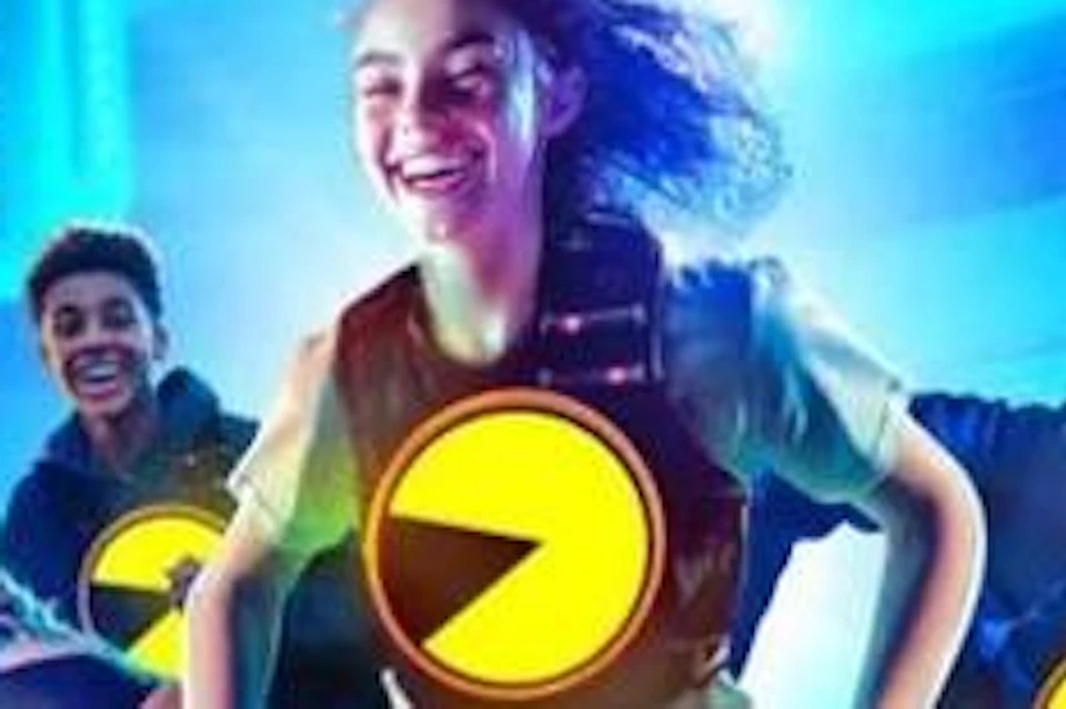 Five people with large yellow Pac-Man symbols on their shirts run joyfully in a vibrant, Pac-Man-themed arena.