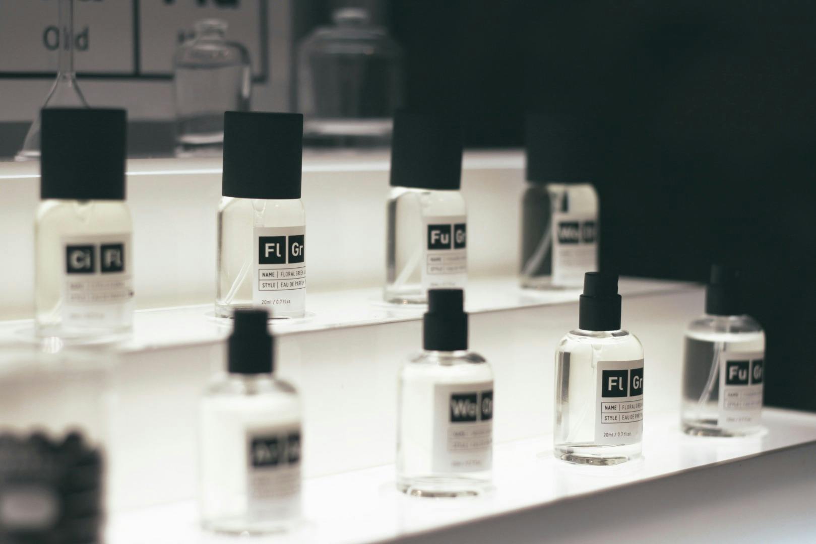 A display of glass perfume bottles with black caps arranged on a white tiered stand, under soft lighting.