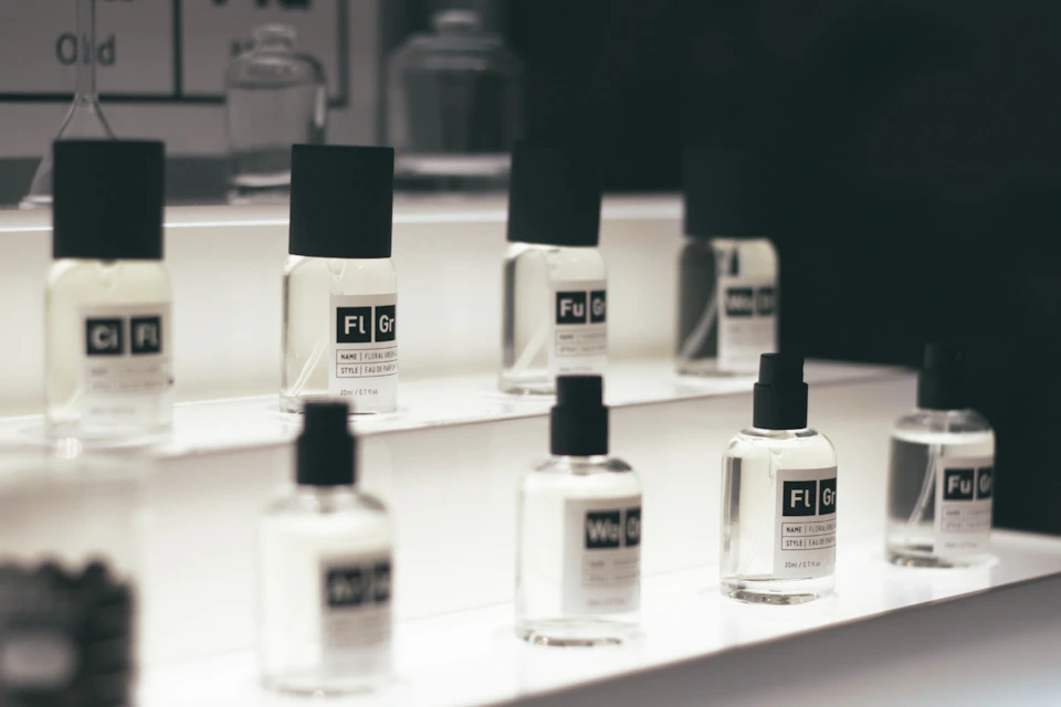 A display of glass perfume bottles with black caps arranged on a white tiered stand, under soft lighting.