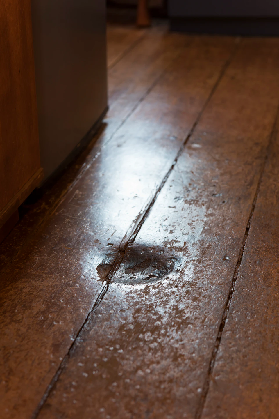 Worn wooden floorboards with a noticeable dent near the center, showing a reflection of light.