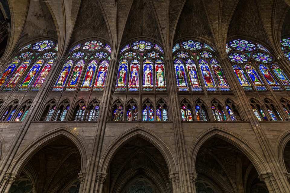 Colorful stained glass windows depicting various scenes and saints in a grand, arched cathedral interior.