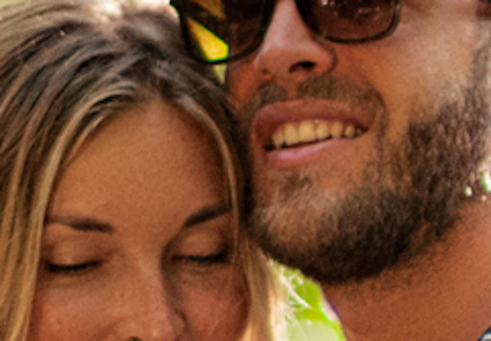 A couple stands under a stone arch surrounded by greenery. The male wears sunglasses; a 'Xplor Hidden Worlds' sign is in the foreground.