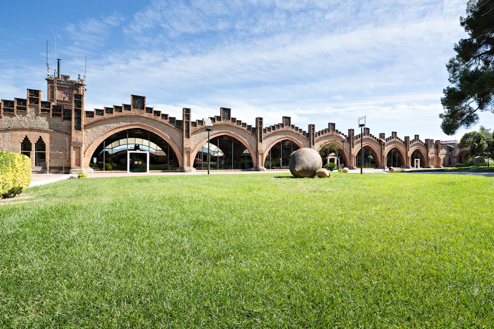 A brick building with arched windows and a grassy lawn in front, under a blue sky with scattered clouds.