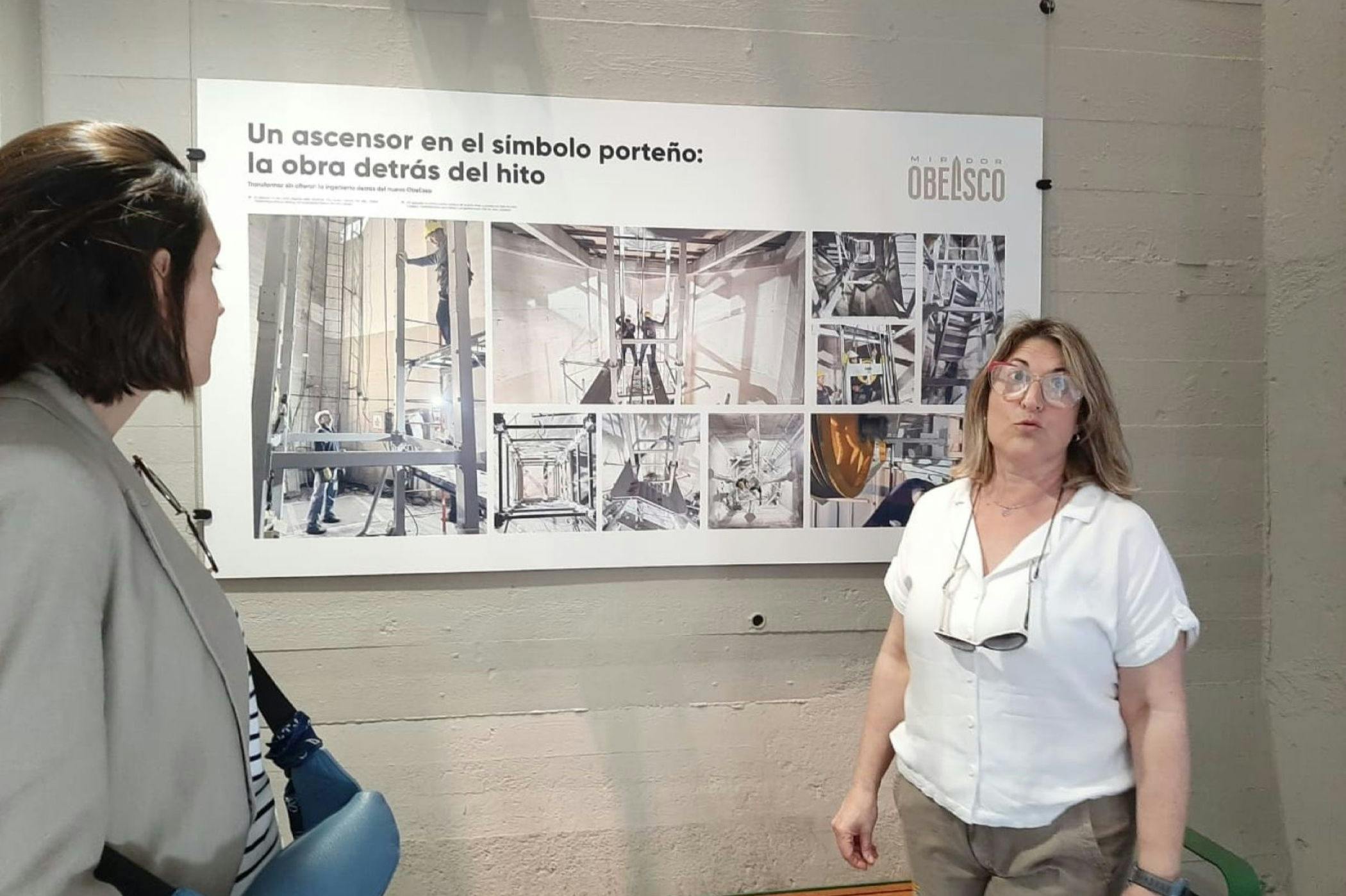 A woman stands in front of a display about the Obelisco, featuring photos and text, in an indoor setting.