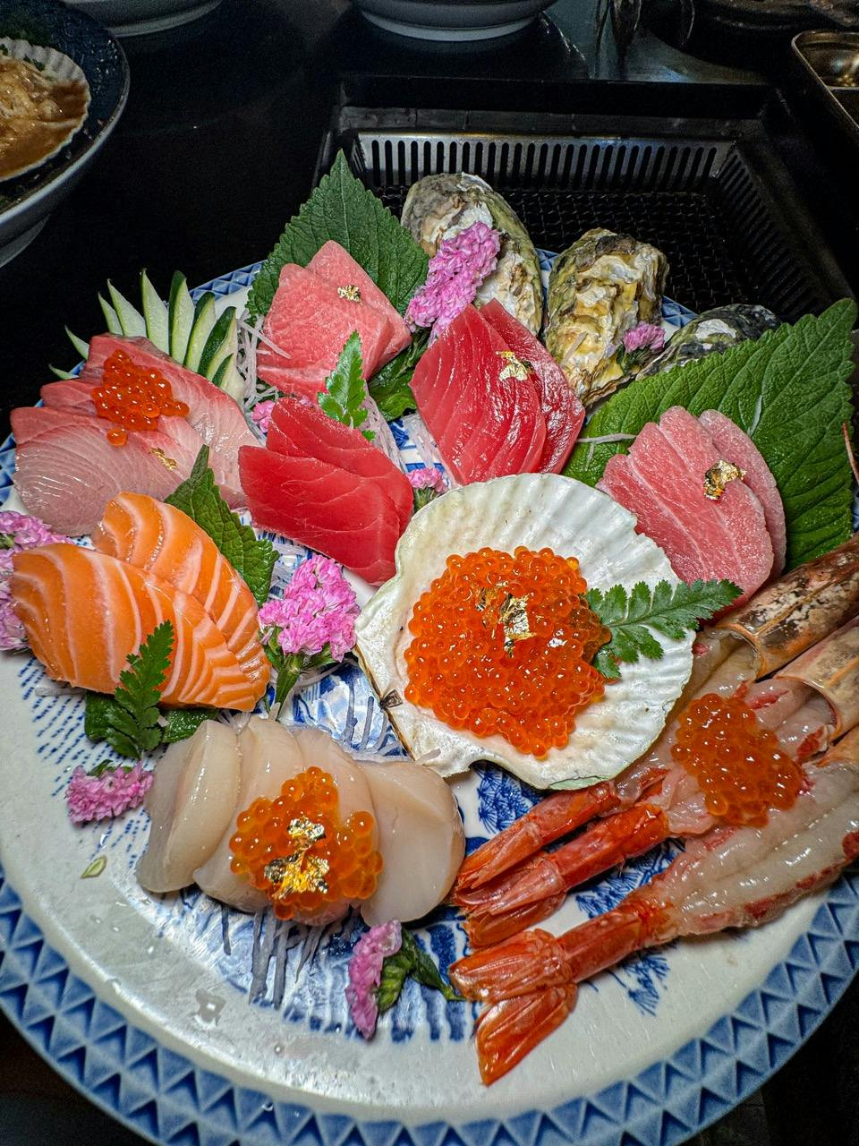 A platter of assorted sashimi with salmon, tuna, shrimp, scallop, roe, and garnishes, served on a decorative plate.