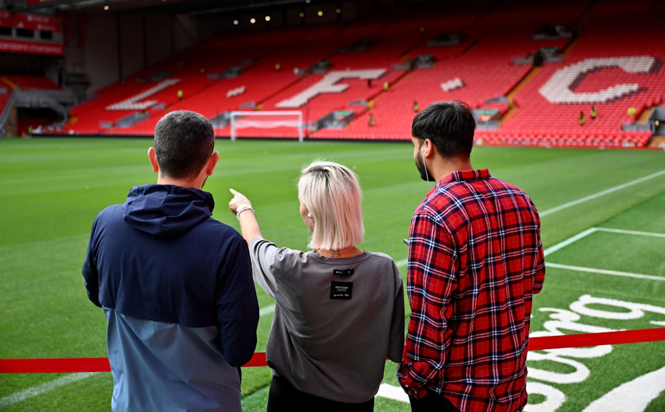 Two people stand near the edge of a soccer field, looking at the empty stadium seats with large white letters.