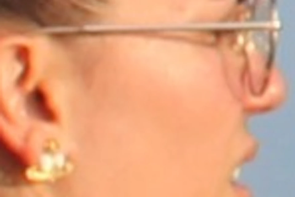 People standing and sitting on a boat's deck, enjoying a view of a calm body of water and distant buildings under a blue sky.