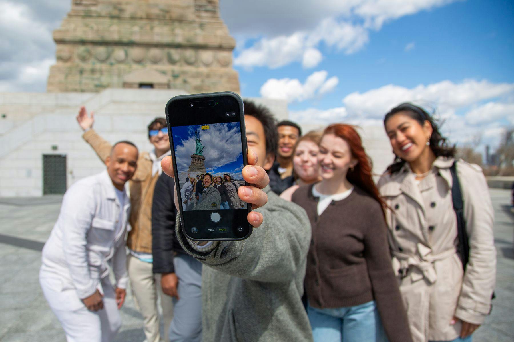 Een groep mensen neemt een selfie voor een monument met een heldere hemel zichtbaar.