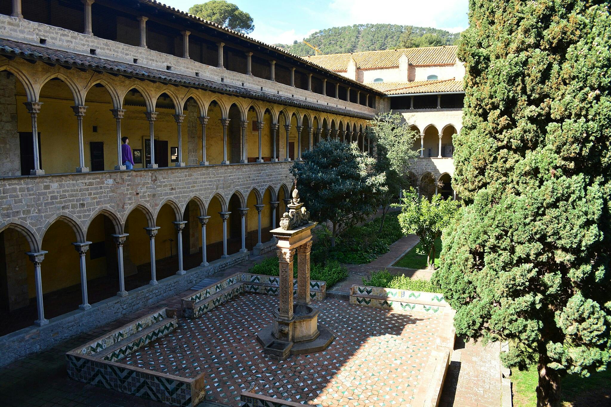 这座宽敞的庭院拥有华丽的喷泉，周围环绕着一栋两层的石头建筑，里面有拱形柱子和郁郁葱葱的绿树。