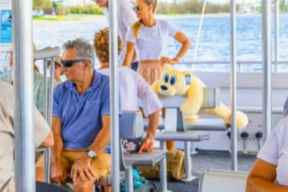 People seated and conversing inside a small ferry boat, with water and trees visible through the open sides.