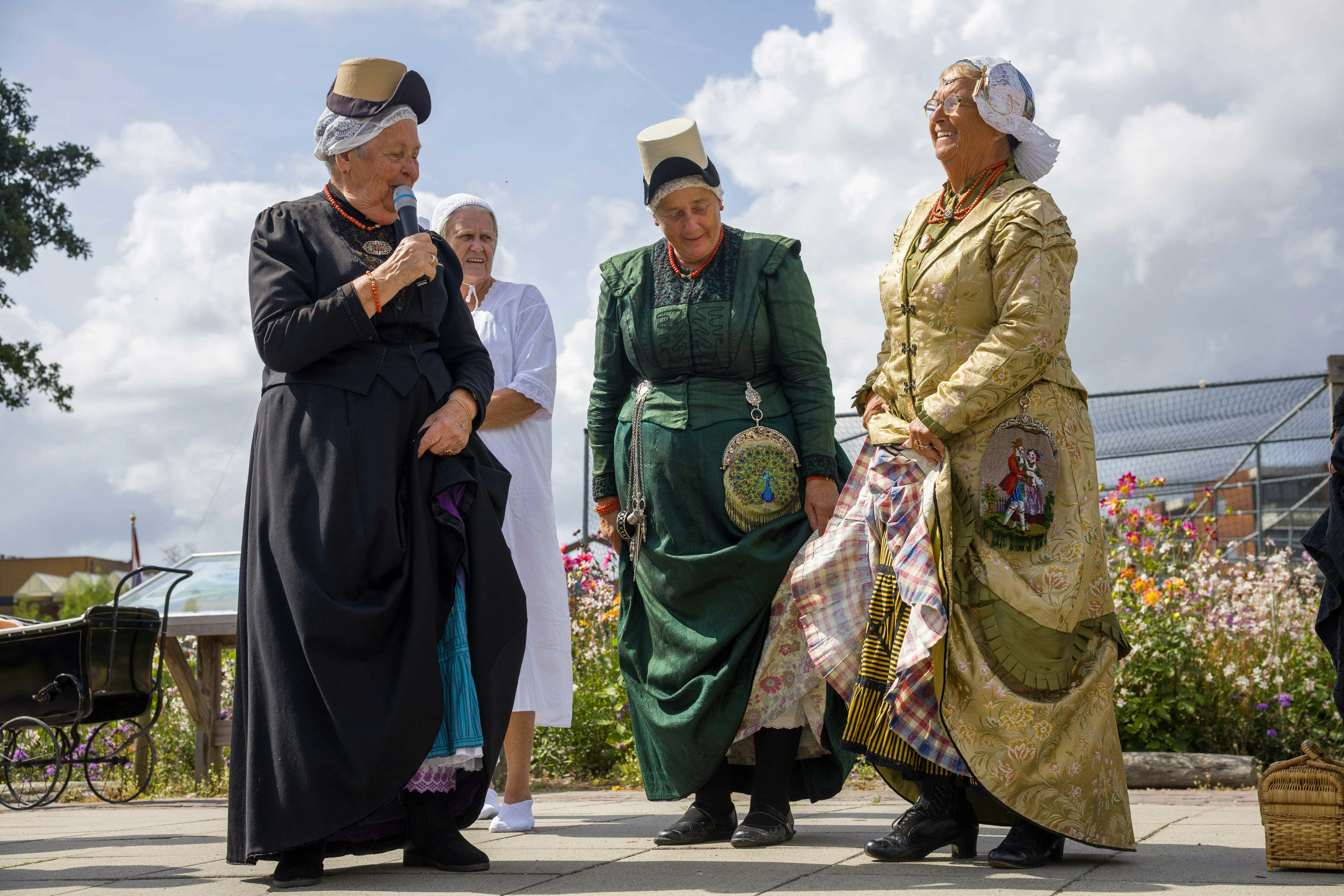Vier traditionell gekleidete Personen stehen im Freien, eine von ihnen spricht in ein Mikrofon.