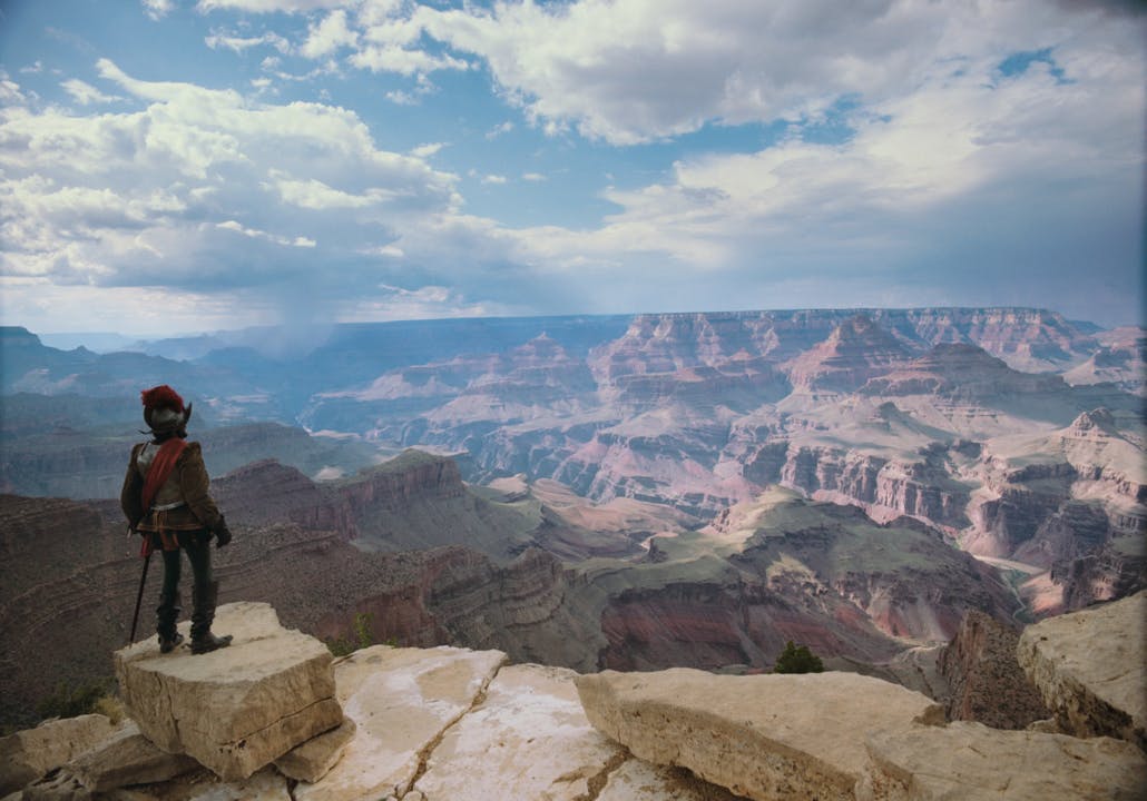 一个人站在岩石悬崖边缘，在一片多云的天空下俯瞰广阔的大峡谷。