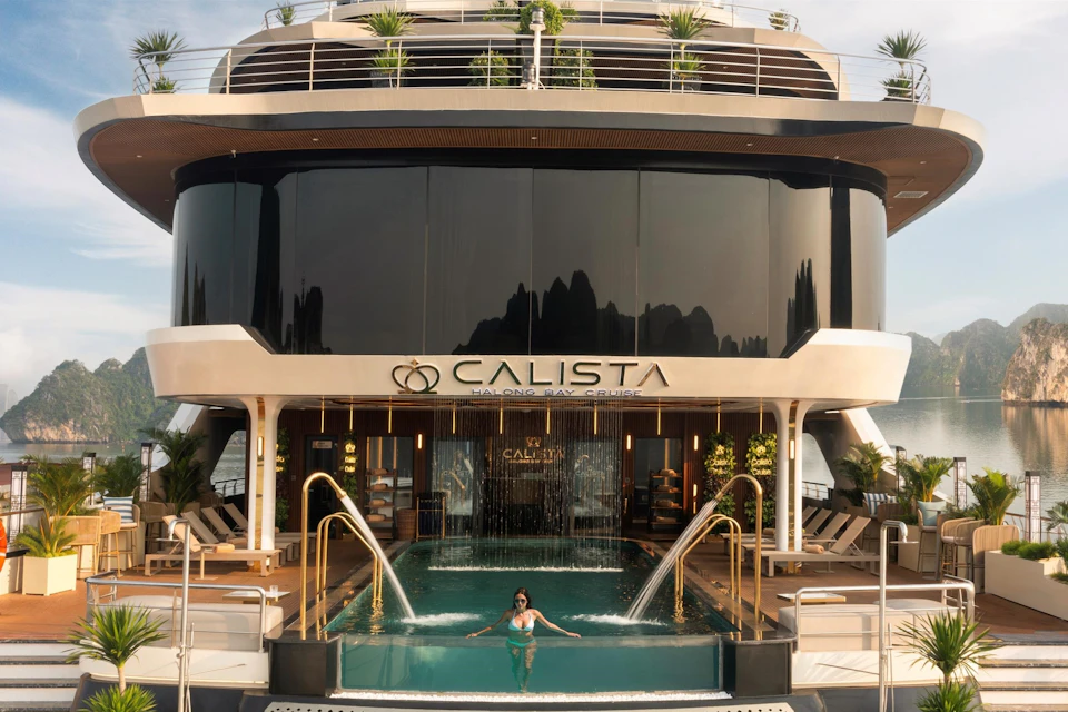Luxurious yacht with a pool and cascading waterfall. A woman swims while lounge chairs and greenery adorn the background. "CALISTA" sign visible.
