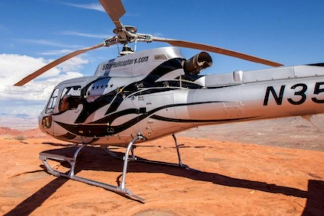 A helicopter with a black and white design parked on a rocky terrain under a clear blue sky.