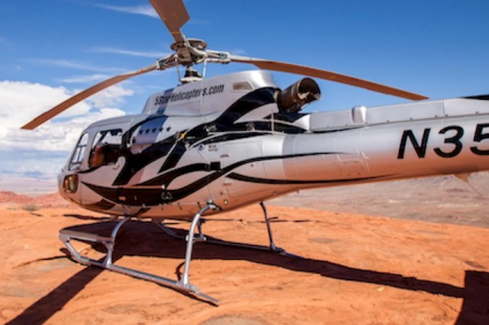 A helicopter with a black and white design parked on a rocky terrain under a clear blue sky.