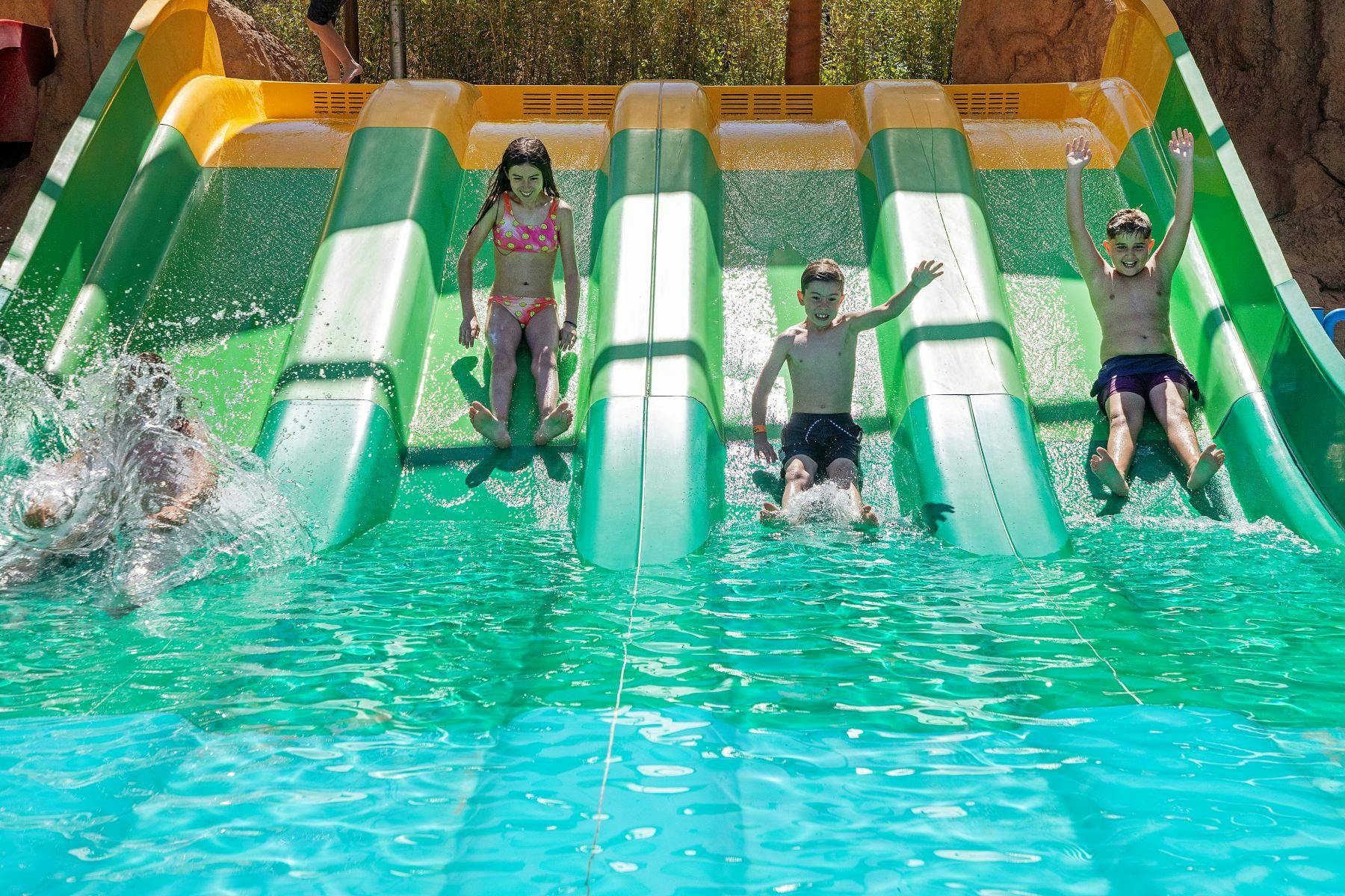 Els nens que es llisquen per l'aigua verda i groga es llisquen a la piscina.
