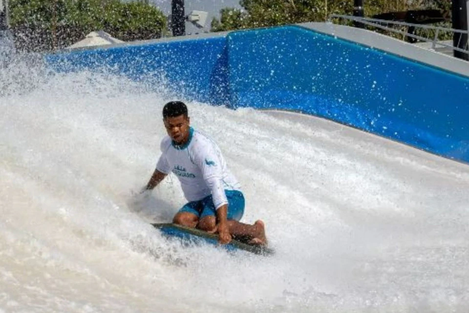 A man in a white outfit rides a wave in a water park on a bodyboard, surrounded by splashing water.