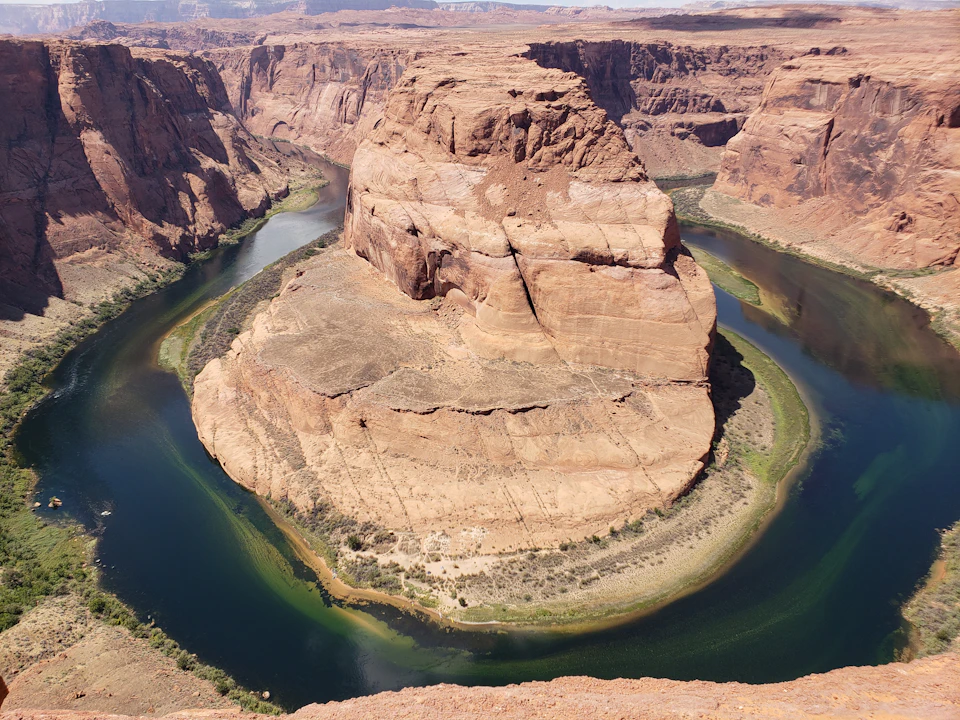 A horseshoe-shaped bend in a river surrounding a large rock formation in a desert landscape.