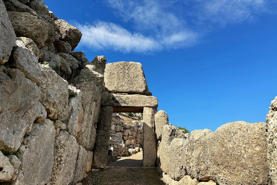 A narrow stone gate with large rectangular blocks under a blue sky, part of Mycenae’s defensive walls.