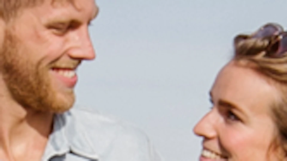 A couple walks through a colorful flower garden, smiling at each other under a clear sky.