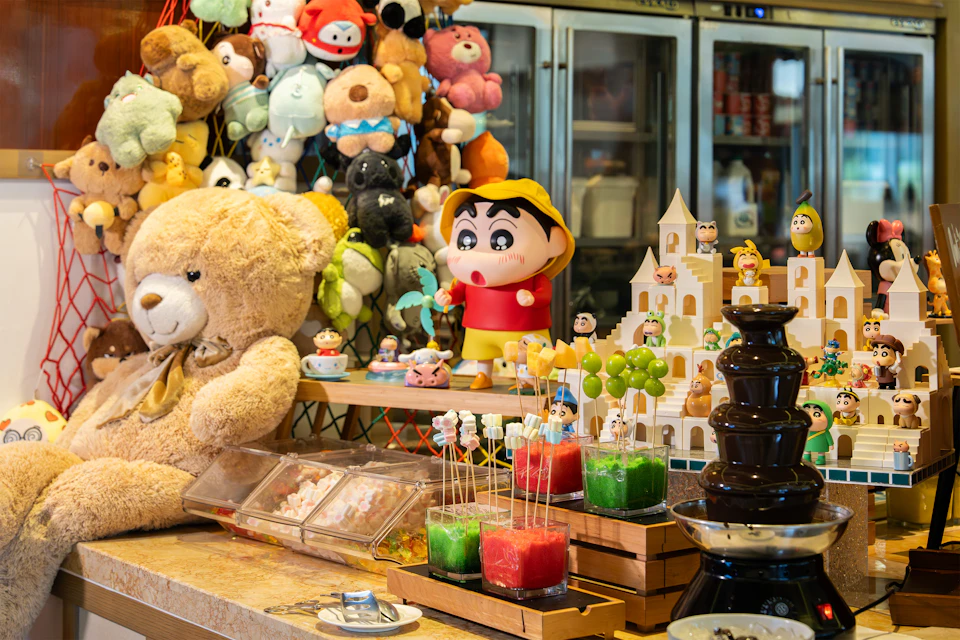A colorful display featuring plush toys, a Shin-chan figure, desserts, and a chocolate fountain in a cozy setting.
