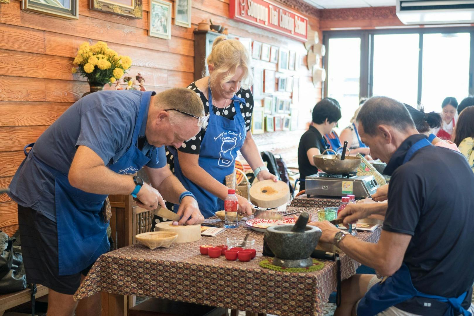 People wearing aprons participate in a cooking class, preparing ingredients on tables in a bright room.