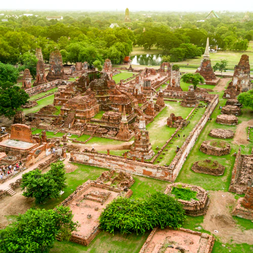 Luftaufnahme der alten Tempelruinen, umgeben von üppigem Grün und Bäumen, mit verstreuten Besuchern, die die Stätte erkunden.