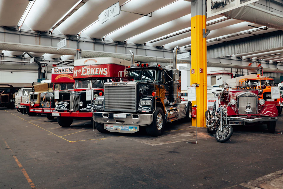 A collection of large trucks and a motorcycle displayed indoors in a well-lit exhibition space with industrial decor.